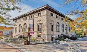 Fort Collins Museum of Art, a historic two-story limestone building with Romanesque Revival architecture featuring arched windows, decorative cornice, and banners, surrounded by autumn trees